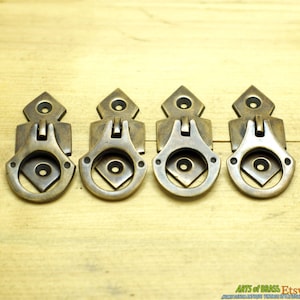 May include: Four antique brass drawer pulls with a ring handle and a decorative diamond-shaped plate. The pulls are arranged in a row on a wooden surface.