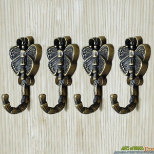 May include: Set of four antique brass butterfly hooks. Each hook features a detailed butterfly design with a black finish and a curved hook.