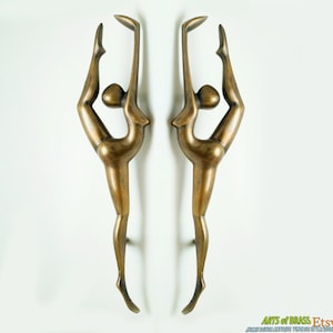Puede incluir: Un par de tiradores de puerta de latón antiguo con forma de bailarina estilizada en un estilo moderno de mediados de siglo.