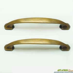 May include: Two antique brass cabinet pulls with a curved design. The pulls have a slightly aged, distressed finish.