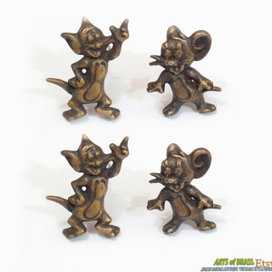 以下が含まれることがあります： 真鍮製のトムとジェリーのヴィンテージフィギュア4体。フィギュアの高さは約5cmで、状態は良好です。トムとジェリーのファンなら、コレクションに加えるのに最適です。