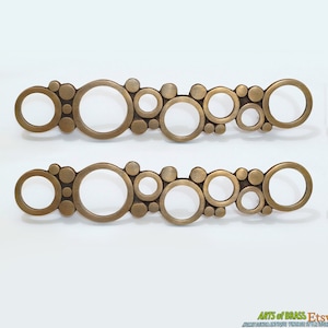 May include: Two brass drawer pulls with a circular design. The pulls are made of a series of interlocking circles of varying sizes.