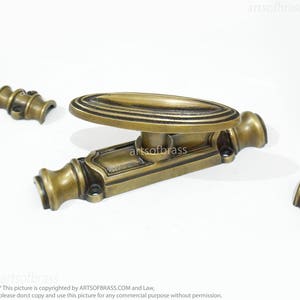 May include: A brass window latch with an oval handle and decorative details. The latch is in a polished brass finish.
