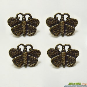 Könnte beinhalten: Satz mit vier antiken Messing-Schubladengriffen in Form von Schmetterlingen. Jeder Griff hat ein detailliertes, strukturiertes Schmetterlingsdesign.