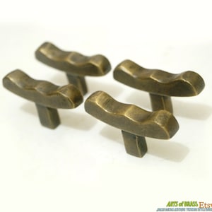 May include: Set of four antique brass cabinet knobs with a wavy, textured design. Each knob has a T-shaped base.