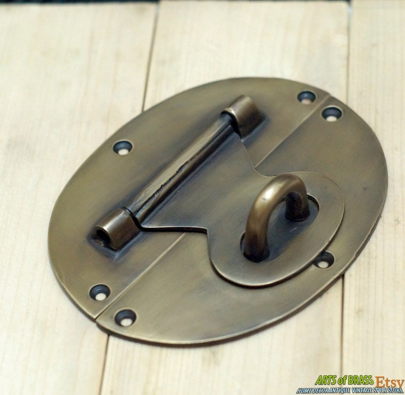 May include: A brass oval-shaped latch with a sliding bolt and a ring handle. The latch has a distressed finish and is suitable for use on a cabinet, chest, or door.
