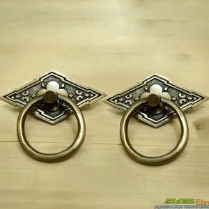 Puede incluir: Dos tiradores de puerta de latón antiguo con un diseño en forma de diamante y un asa de anillo. Los tiradores tienen un patrón floral decorativo y un acabado texturizado.