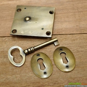 May include: Antique brass keyhole escutcheon set with a key. The set includes a square escutcheon, two oval escutcheons, and a key with a heart-shaped hole. The escutcheons have a distressed finish and are perfect for adding a vintage touch to any project.