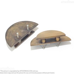 May include: Two brass cabinet door pulls in the shape of half circles. The pulls are stacked on top of each other. The top pull is slightly larger than the bottom pull. Both pulls have two screws for installation.