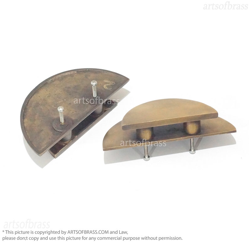 May include: Two brass cabinet door pulls in the shape of half circles. The pulls are stacked on top of each other. The top pull is slightly larger than the bottom pull. Both pulls have two screws for installation.