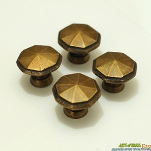 May include: Four antique brass cabinet knobs with a geometric, starburst design. Each knob has a raised, octagonal shape with a smooth, polished finish.