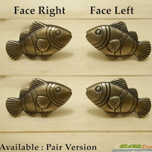 Peut inclure: Quatre boutons de porte en forme de poisson en laiton, deux orientés vers la droite et deux orientés vers la gauche. Les boutons sont détaillés avec des lignes et un œil en relief. Les boutons sont sur une surface en bois. Le texte "Face Right", "Face Left", "Available: Pair Version", "ARTS of BRASS Etsy", et "HOME DECORANTIQUE VINTAGESTYALSTORE" est visible sur l'image.