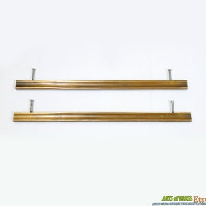 May include: Two brass drawer pulls with a wavy design and silver screws. The pulls are approximately 10 inches long.