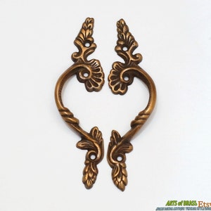 Puede incluir: Un par de tiradores de puerta de latón ornamentados con un diseño en forma de corazón y detalles florales intrincados.
