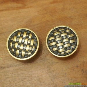 Może przedstawiać: Dwa okrągłe mosiężne gałki do szafki z wzorem plecionym. Gałki są ciemno mosiężne z plecionym wzorem w kolorze złotym.