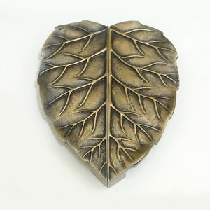 May include: A gold leaf-shaped decorative object with a detailed vein pattern. The leaf is made of metal and has a slightly textured surface.