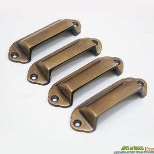 Peut inclure: Quatre poignées de tiroir en laiton antique de forme rectangulaire légèrement arrondie. Les poignées ont un bord légèrement surélevé autour du périmètre et une finition lisse et polie.