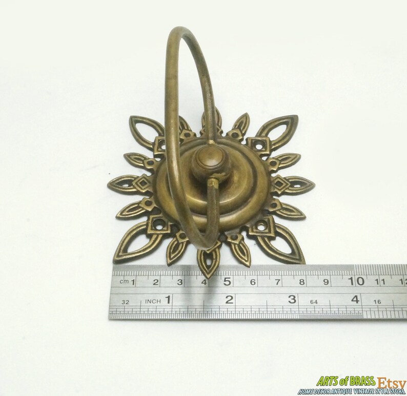 May include: Brass wall hook with a decorative sunburst design and a ring for hanging items. The hook measures approximately 2 inches in diameter.