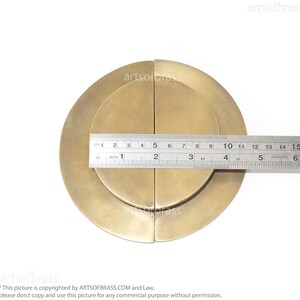 May include: A pair of round, brass door handles with a concentric circle design. The handles are 4 inches in diameter.