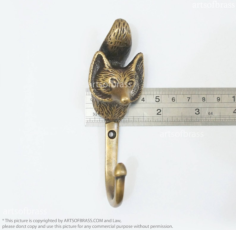 May include: Brass fox head coat hook with a 3-inch hook. The hook is measured against a ruler.