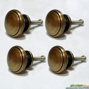 May include: Four antique brass cabinet knobs with a raised rim and a screw. The knobs are approximately 1 inch in diameter.