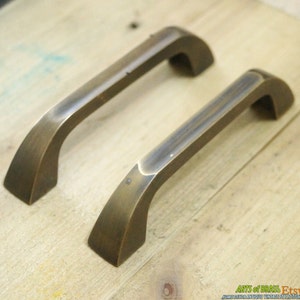 May include: Two antique brass cabinet door pulls with a curved design. The pulls are made of solid brass and have a brushed finish.