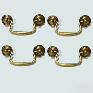 May include: Four antique brass cabinet pulls with a rounded, decorative design. Each pull has a curved handle and a round knob on each end.