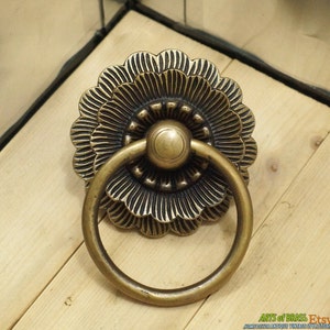 May include: A brass door pull with a decorative floral design. The pull has a ring handle and a detailed floral pattern.