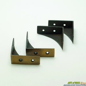 May include: Four antique brass corner brackets with two holes each. The brackets are made of metal and have a dark patina finish.