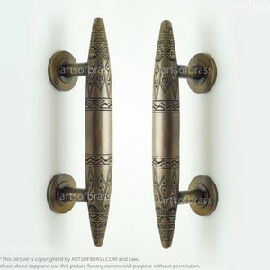 Puede incluir: Dos tiradores de puerta de latón antiguo con intrincados diseños geométricos. Los tiradores tienen forma de lágrima alargada con la parte superior redondeada y la inferior puntiaguda. Los tiradores están unidos a placas redondas.