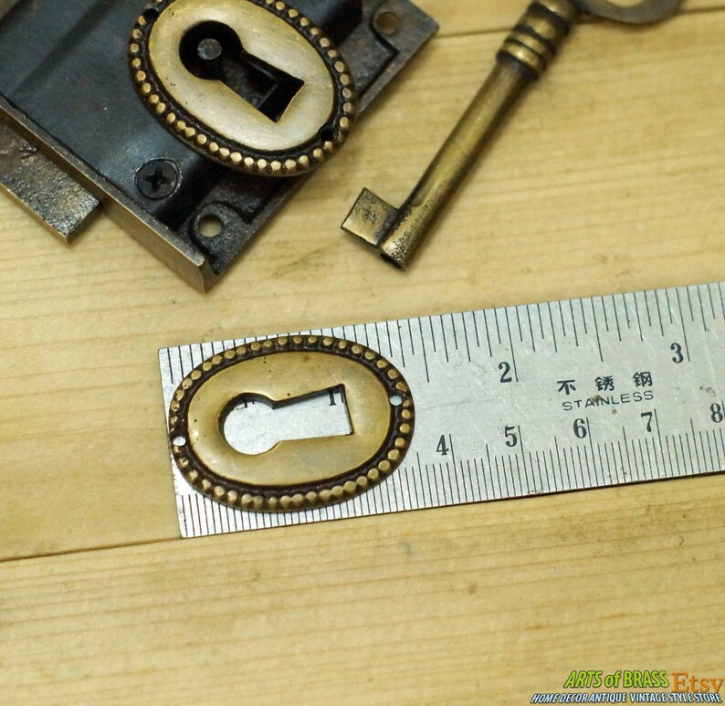 May include: A close-up of a brass keyhole cover with a decorative beaded edge. The cover is 1 1/2 inches in diameter and is measured against a ruler.
