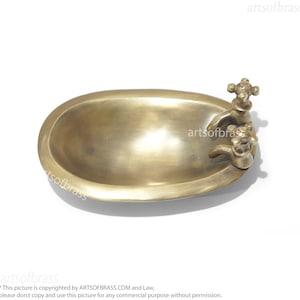 May include: A small, oval-shaped brass bathtub with two brass faucets. The bathtub is a decorative item and is not functional.