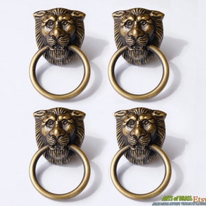 May include: Four antique brass lion head drawer pulls with ring handles. Each pull features a detailed lion head with a textured finish.