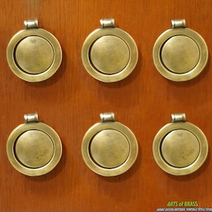May include: Six antique brass door knobs with a circular design and a raised outer ring. The knobs are mounted on a wooden surface.