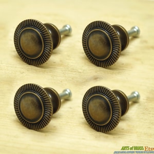 May include: Four antique brass cabinet knobs with a sunburst design. Each knob has a round, slightly domed top with a raised, textured rim. The knobs are attached to a screw.