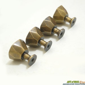 May include: Four antique brass cabinet knobs with a geometric, faceted design. Each knob has a threaded screw post for installation.