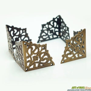 May include: Four ornate brass corner brackets with a decorative floral design. The brackets are separated and laid out in a square shape.
