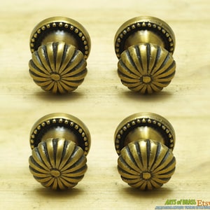 Könnte beinhalten: Vier antike Messing-Schrankknöpfe mit Sonnenstrahlen-Design. Jeder Knopf hat einen perlenbesetzten Rand und eine geriffelte, abgerundete Oberseite.