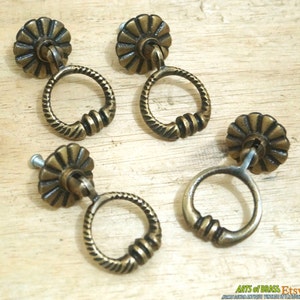 May include: Four antique brass cabinet knobs with a decorative ring pull and a flower-shaped top. The knobs are on a wooden surface.