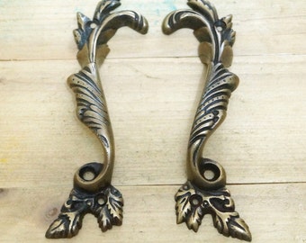 May include: A pair of ornate brass door pulls with a leaf design. The pulls are in a vintage style and have a warm, aged finish.