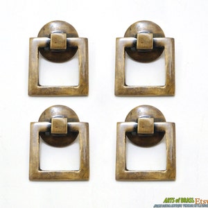 May include: Four antique brass square cabinet drawer pulls with a ring handle. Each pull has a round base and a square frame.