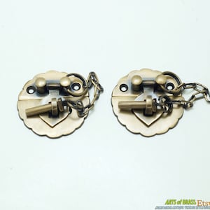 Puede incluir: Dos cierres de corazón de latón antiguo con una cadena y una llave. Los cierres son ornamentados y tienen un diseño decorativo.