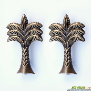 Puede incluir: Dos tiradores de puerta de palmera de latón antiguo. Las palmeras están detalladas con hojas texturizadas y un tronco trenzado.