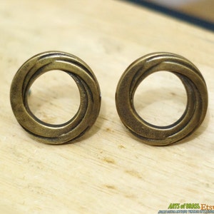 May include: Two brass cabinet knobs with a circular design. The knobs have a concentric circle pattern with a smooth, polished finish.