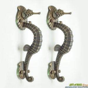 Könnte beinhalten: Zwei verzierte Türgriffe aus Messing in Form von Seepferdchen. Die Griffe sind mit strukturierten Schuppen verziert und haben eine grüne Patina-Oberfläche.