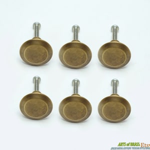 May include: Six antique brass cabinet knobs with round bases and silver screws. The knobs have a distressed, aged finish.