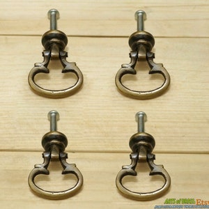 May include: Set of four antique brass cabinet knobs with a decorative design. Each knob has a ring pull and a screw for installation.