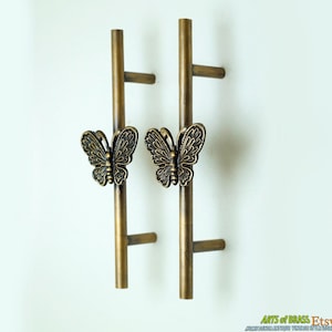 Könnte beinhalten: Zwei antike Messing-Türgriffe mit Schmetterlingsförmigen Griffen. Die Griffe sind etwa 15 cm lang und haben ein schlichtes, elegantes Design.