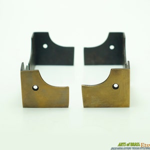 Könnte beinhalten: Zwei Eckwinkel aus Messing mit schwarzer Metallbeschichtung. Die Winkel sind als Eckstützen für Möbel oder andere Projekte konzipiert.