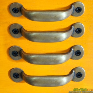May include: Four antique brass drawer pulls with a rounded rectangular shape and a screw on each end. The pulls are arranged in a row on a bright orange surface.